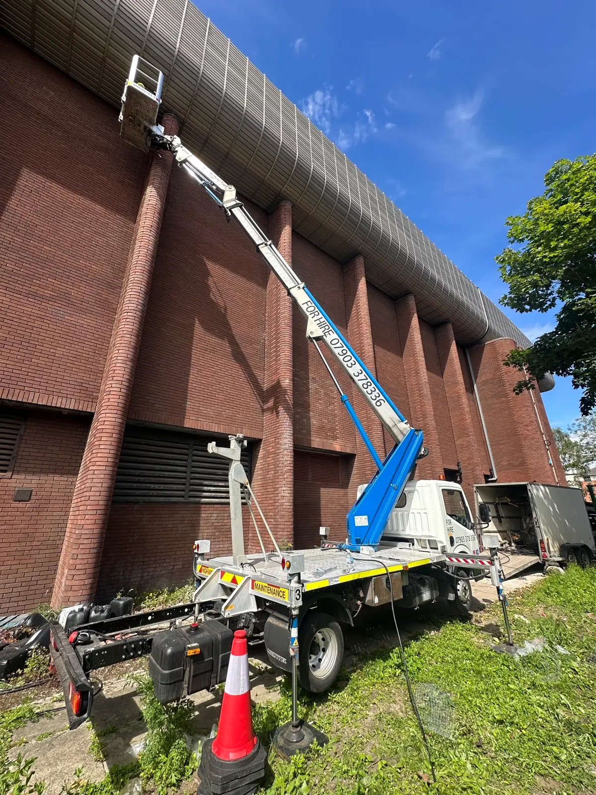 Cherry picker boom fully extended reaching the top of a tall brick building