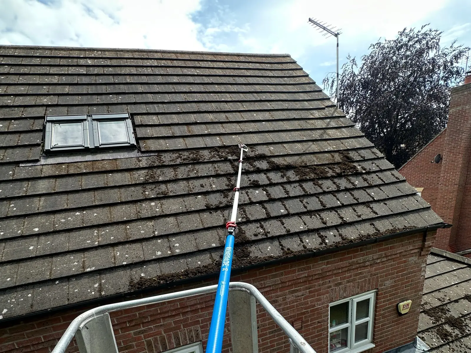 Moss being scraped off roof tiles with a pole, worked from the cherry picker platform